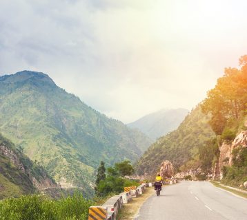 Himalayas landscape with two cyclist, mountains, road, river and clouds