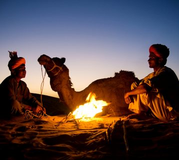 Indian men resting by the bonfire with their camel