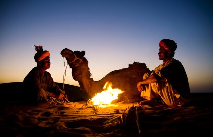 Indian men resting by the bonfire with their camel